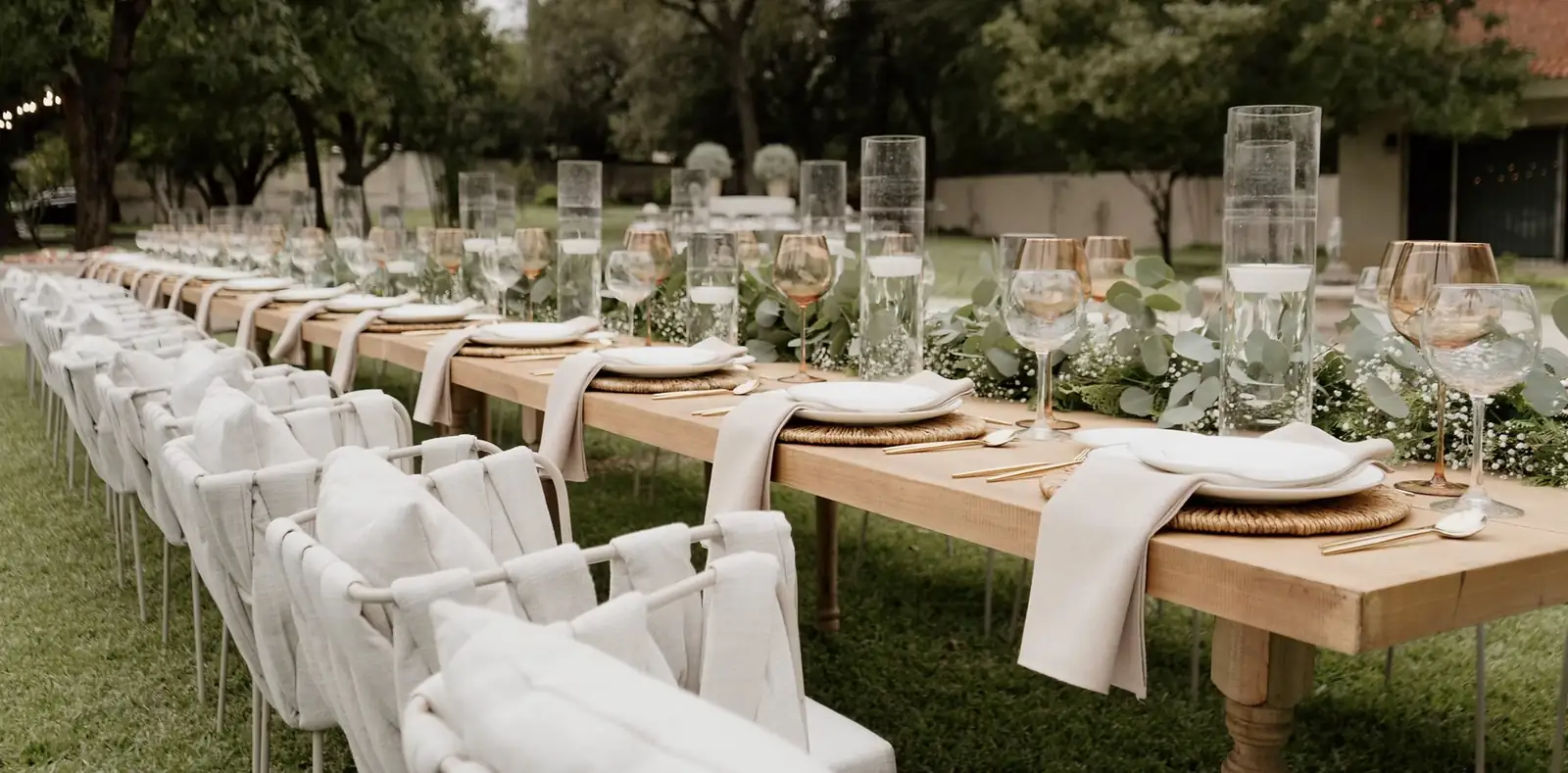 Mesa larga de jardín con mantelería de lino, copas ámbar y centros de eucalipto